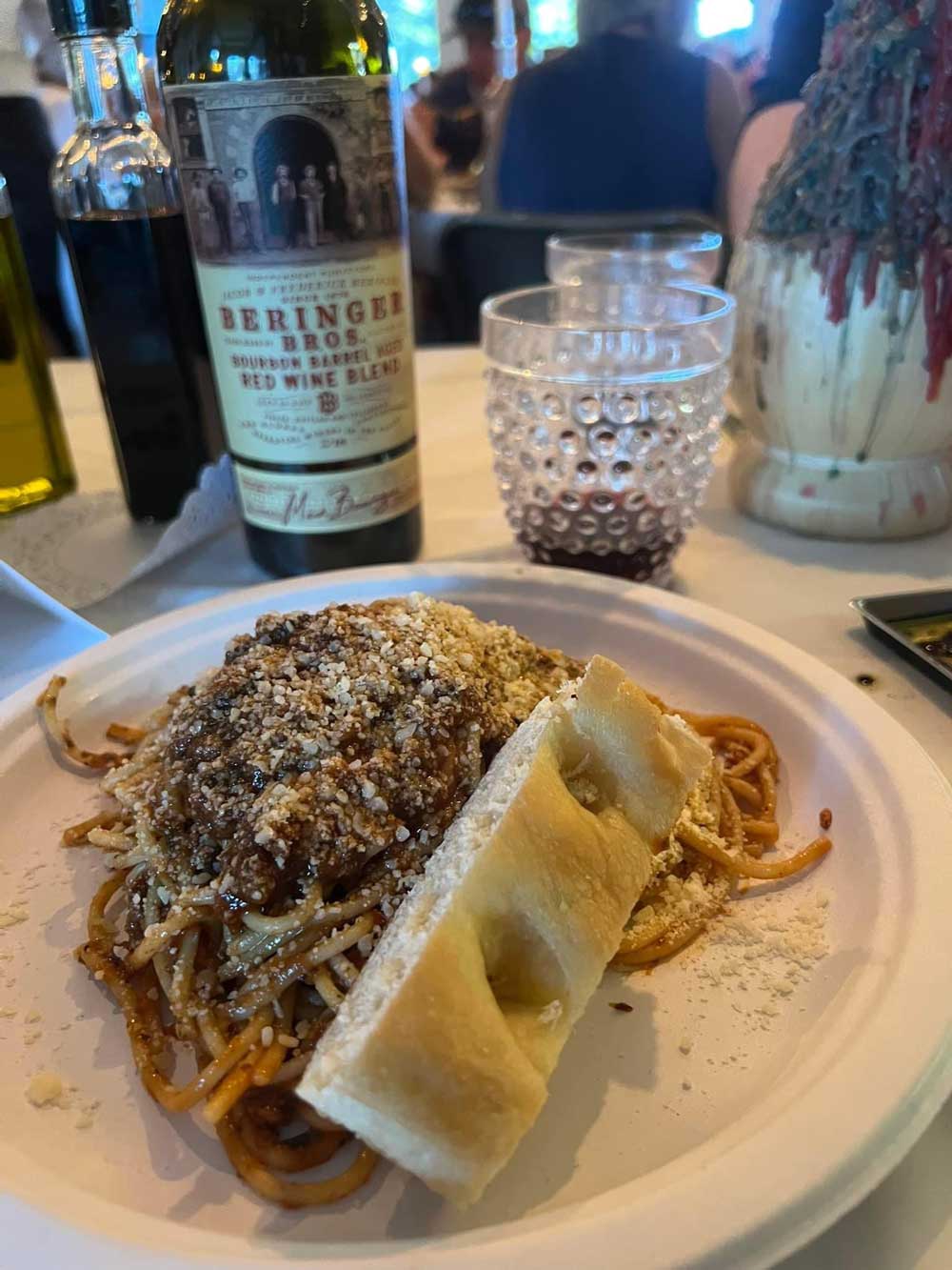 plate of spaghetti with breadstick and wine in background